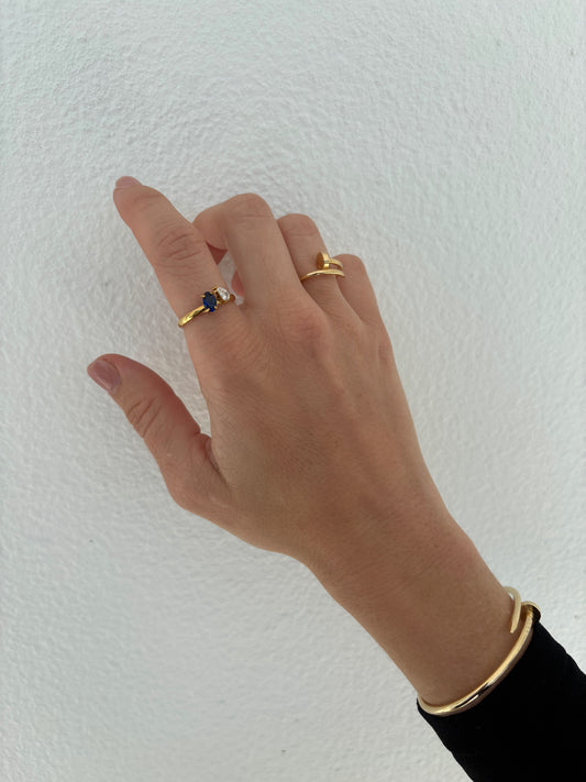 Hand wearing two gold rings with a blue stone on a white background