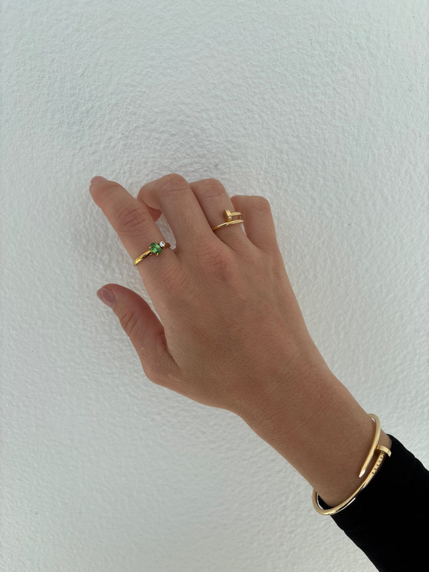 Hand wearing gold rings and a bracelet on a light background