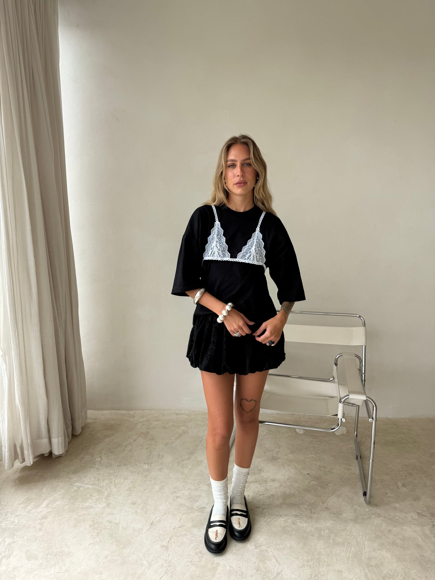 Woman wearing a black outfit with lace details in a minimal room.