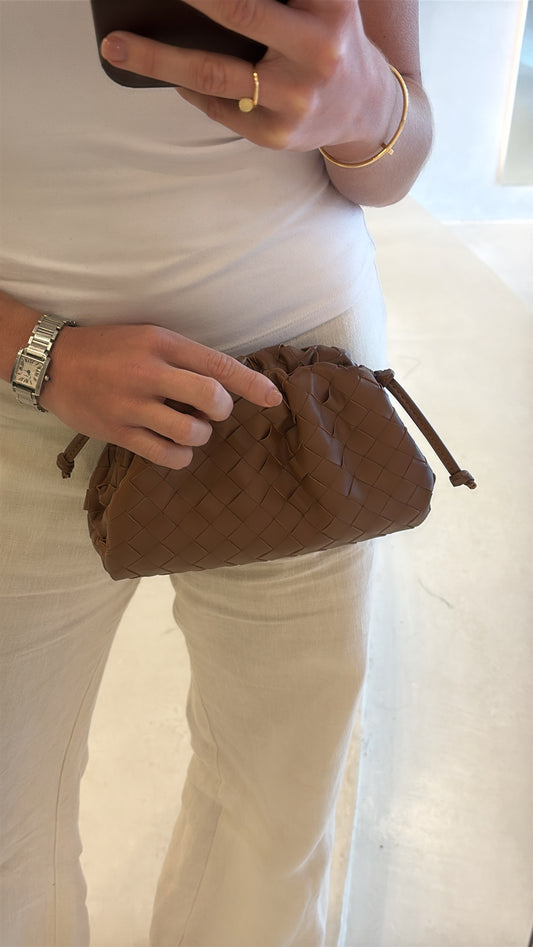 Person holding a brown quilted handbag with a white background
