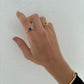 Hand wearing two gold rings with a blue stone on a white background